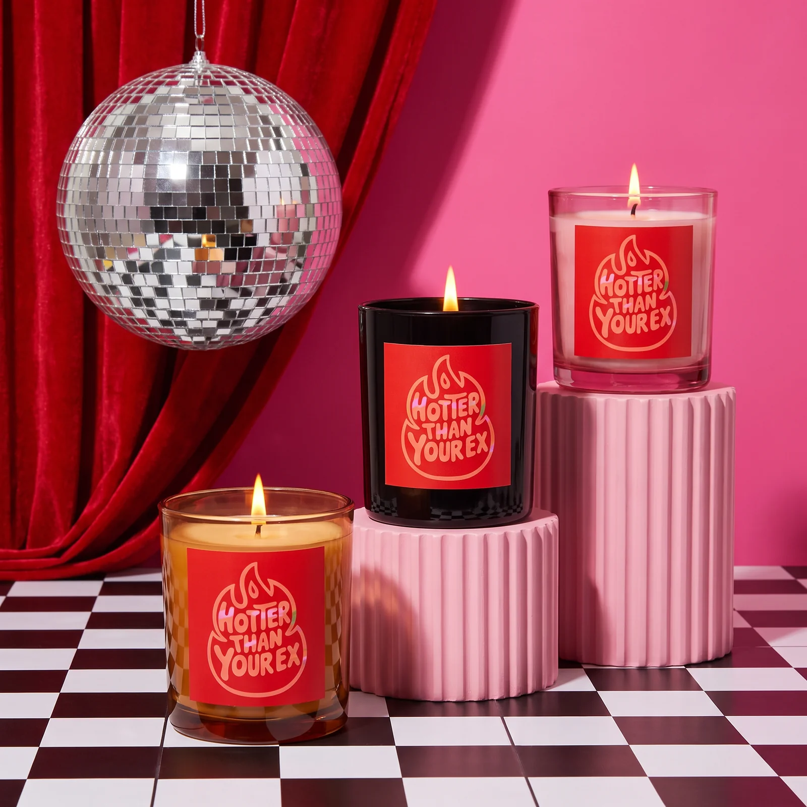 Three Hotter Than Your Ex candles on pink plinths, with a mirror ball, red velvet curtains and a checkerboard floor.